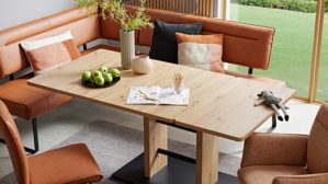 Auszugstisch interliving aus hellem Holz, Ecksofa in Lederoptik in dunklem orange im Hintergrund