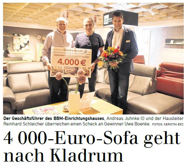 BBM Gewinner eines 4000 Euro Sofas; Drei Männer schauen lächelnd in die Kamera, während zwei den Gutschein hochhalten