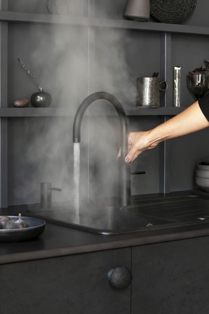 Schwarzer Quooker an einer schwarzen Spüle, Wasser fließ und es qualmt; Symbol für das Heißwasser