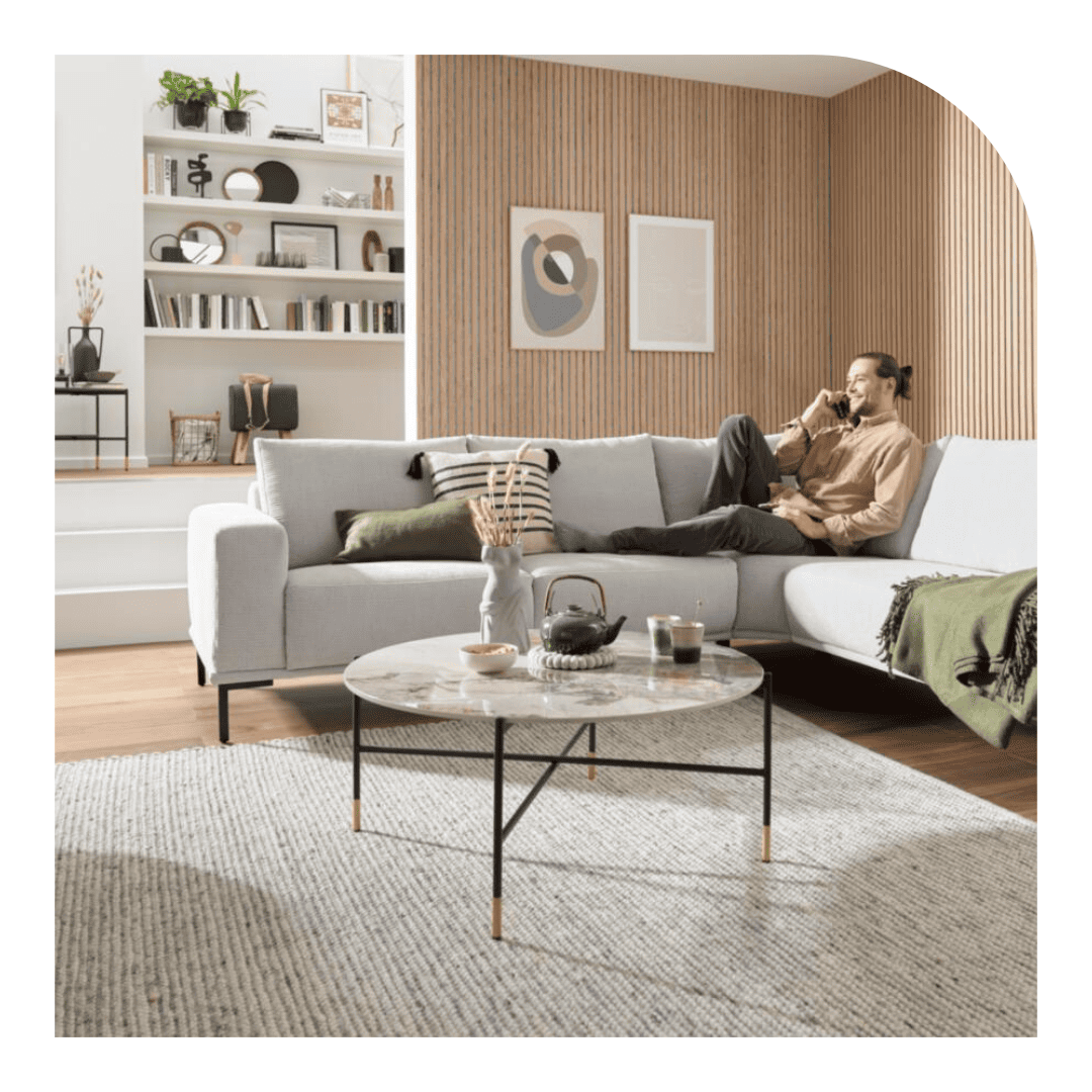 Graues, modernes Ecksofa,auf welchem ein Mann am sitzen und telefonieren ist, im Hintergrund sind holzfarbigen Paneele zu sehen