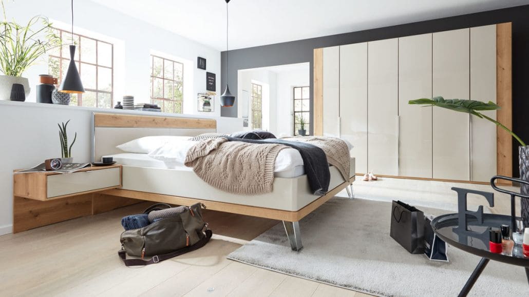 Helles Schlafzimmer, mit holzfarbigem Bett und einem weiß, holzfarbigem Schrank im Hintergrund