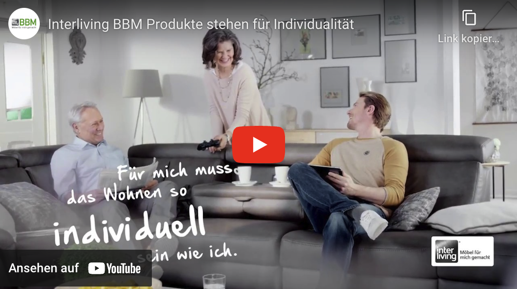 2 Männer auf einem Sofa, eine Frau bringt ihnen Kaffee