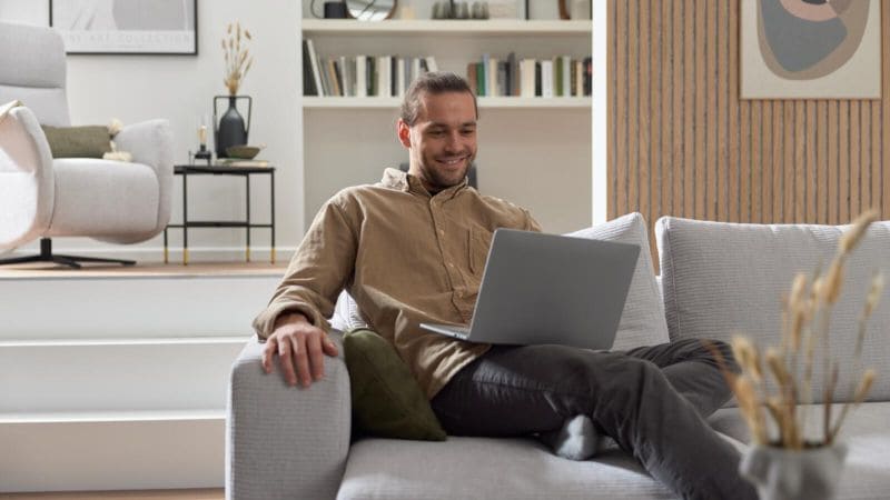 Mann, der mit einem PC auf dem Sofa sitzt und lacht
